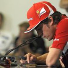 Alonso juega con su iPhone durante la rueda de prensa de la FIA