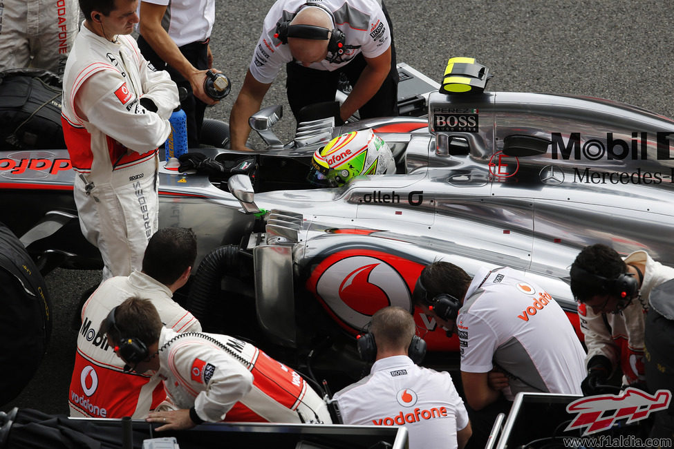 Los mecánicos de McLaren examinan el coche de Pérez en la parrilla